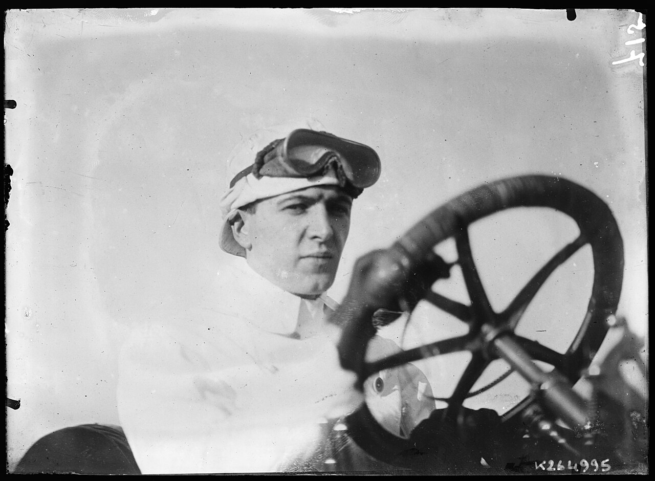 The January 24, 1905 period photograph identifies Arthur Macdonald at the wheel of his Napier in Florida; the profile's primary sources tie Macdonald's record run to Napier L48. The frame is a driver-and-steering-wheel detail, not a full-car portrait.