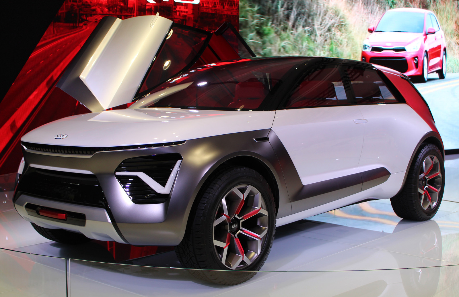 Clear front three-quarter view of the physical silver/white HabaNiro, dark front cladding, distinctive lamps, red C-pillar and far-side raised butterfly door. Display-floor reflections and background screen remain. Not a production Niro and not proof of proposed powertrain or autonomy. Whole image resized and JPEG re-encoded; derivative retains CC BY-SA 4.0.