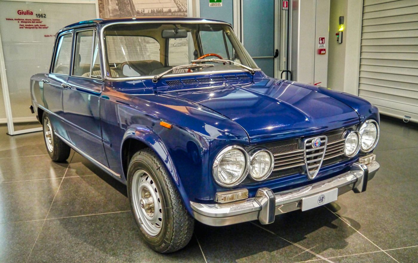 The museum display identifies the car as a 1962 Giulia, but the Commons category also references TI Super. The image supports the first-series Giulia body and year display; it does not independently prove baseline TI trim, original launch brakes, market or restoration originality.