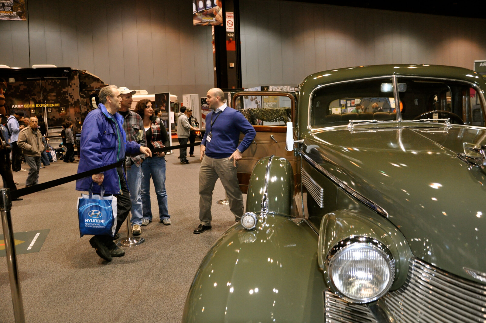 Olive-drab 1938 Cadillac Model 75 Army staff car displayed at the 2012 Chicago Auto Show, viewed from the front right with visitors gathered beside it.