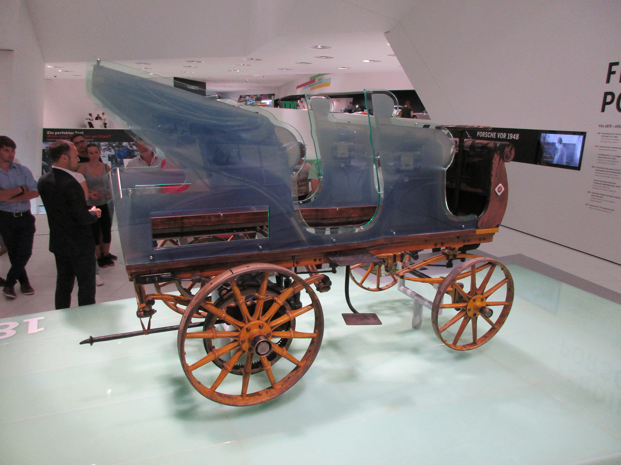 The actual surviving 1898 Egger-Lohner C.2 Phaeton displayed at the Porsche Museum with its timber chassis, four wooden wheels and transparent interpretive body visible.
