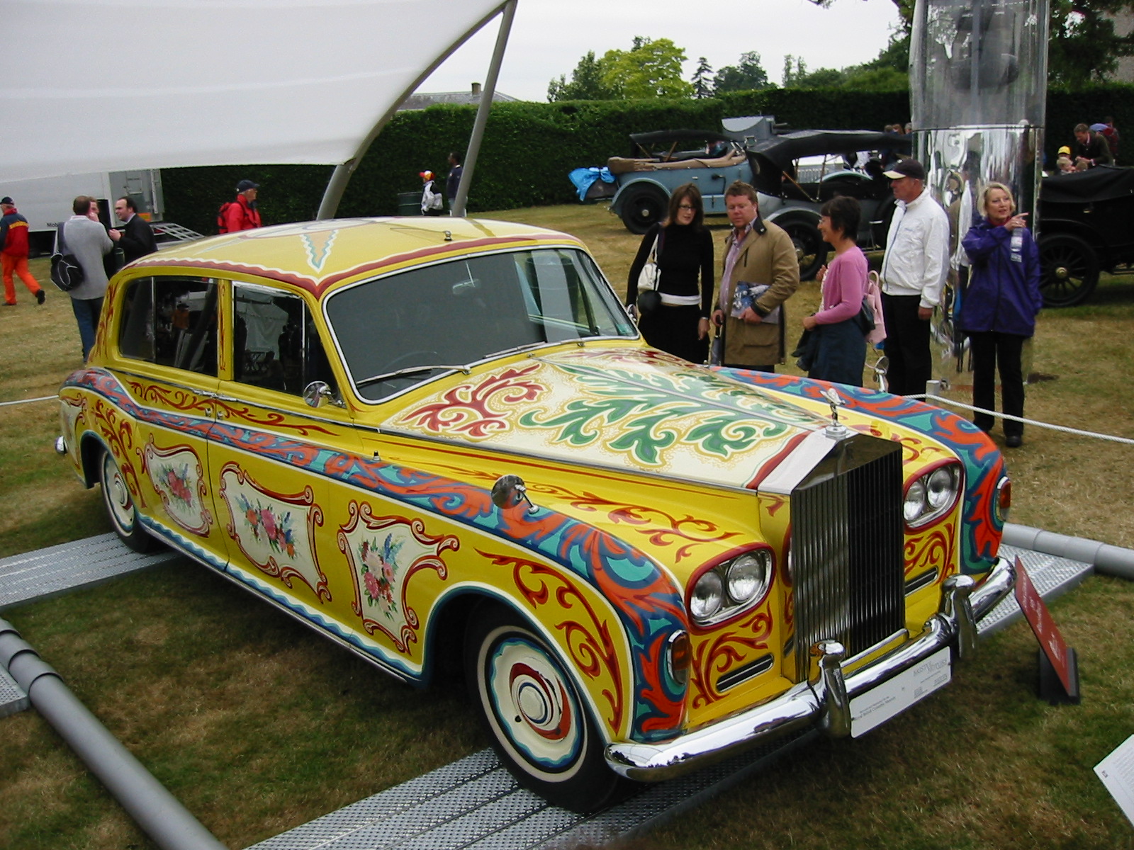 Full front three-quarter view of John Lennon’s yellow floral Rolls-Royce Phantom V, with both bumpers and the visible wheels inside the frame.