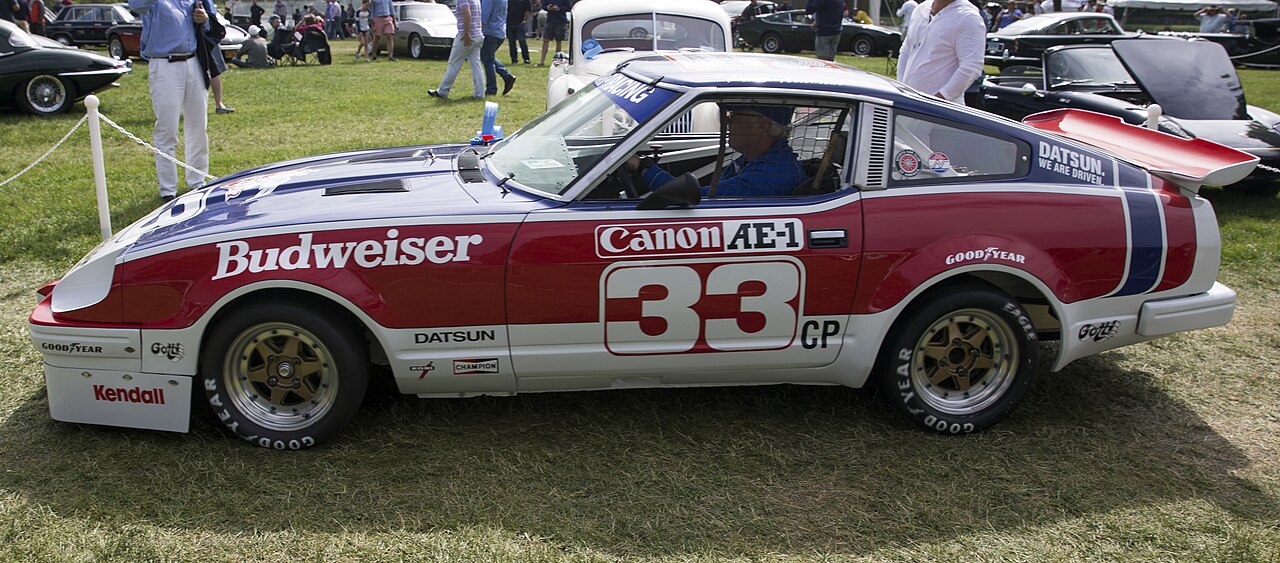 Side view of Paul Newman’s actual red, white and blue no. 33 Datsun 280ZX championship race car at the 2018 Greenwich Concours, with no registration visible.