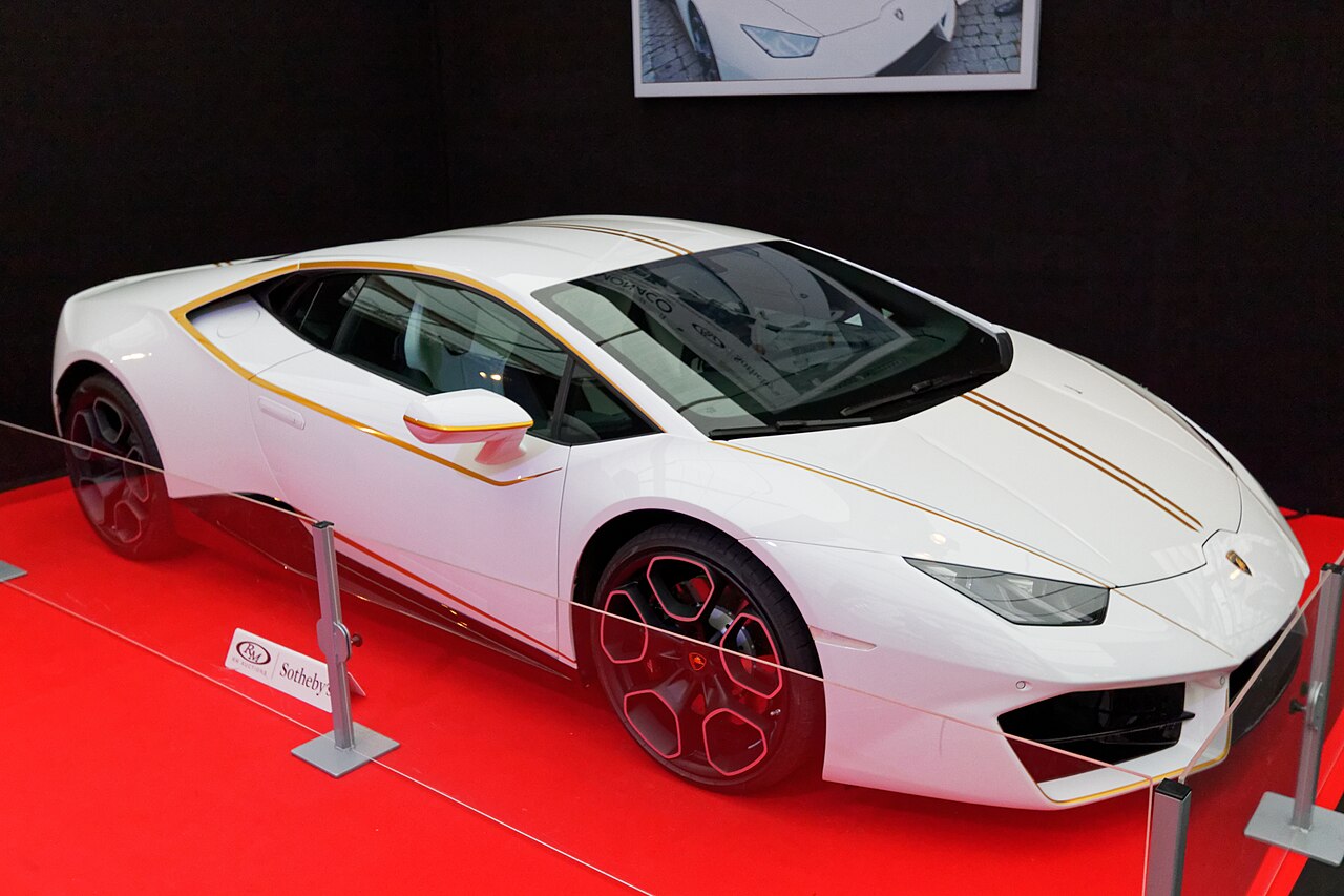 Front-right view of the actual white Pope Francis Lamborghini Huracán with narrow gold stripes at the RM Sotheby's Paris display; no registration is visible.