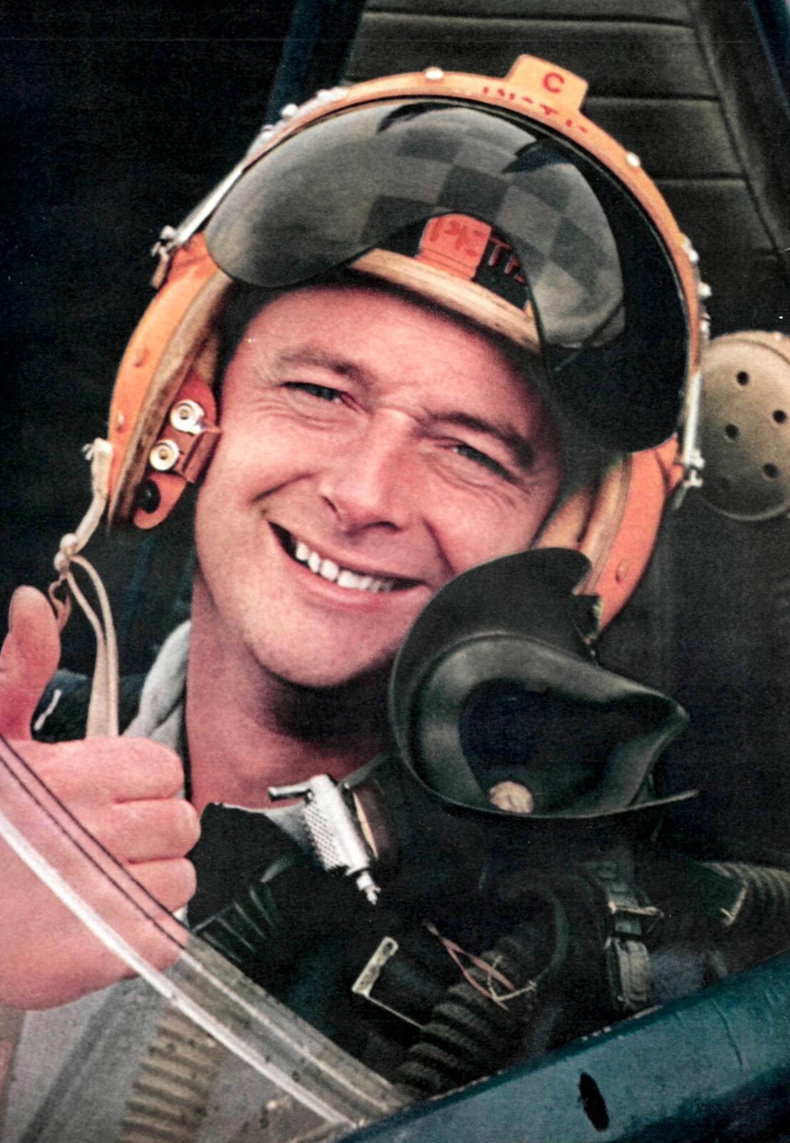 Donald Campbell smiling in a racing helmet and breathing mask while seated in a cockpit in 1957.
