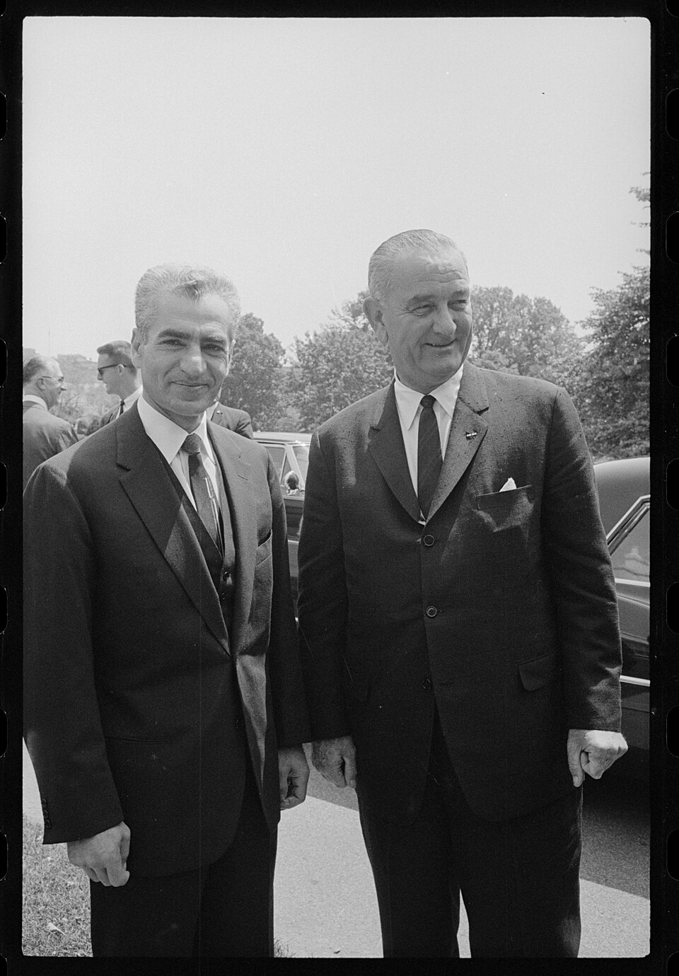 Mohammad Reza Pahlavi standing at left beside U.S. President Lyndon B. Johnson outdoors in June 1964.