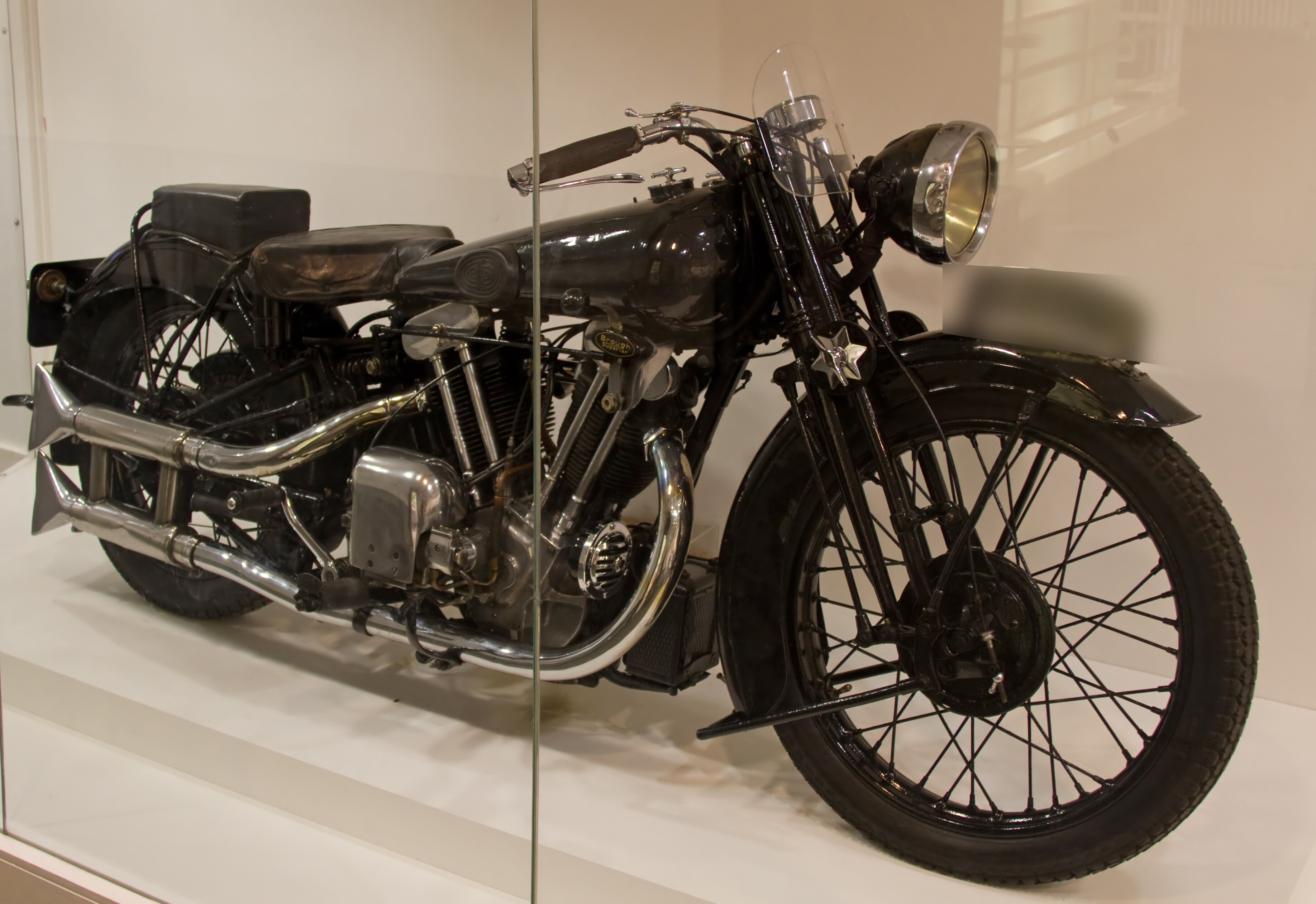 Lawrence’s actual black Brough Superior SS100 George VII displayed behind glass at the Imperial War Museum, with its historic registration obscured.