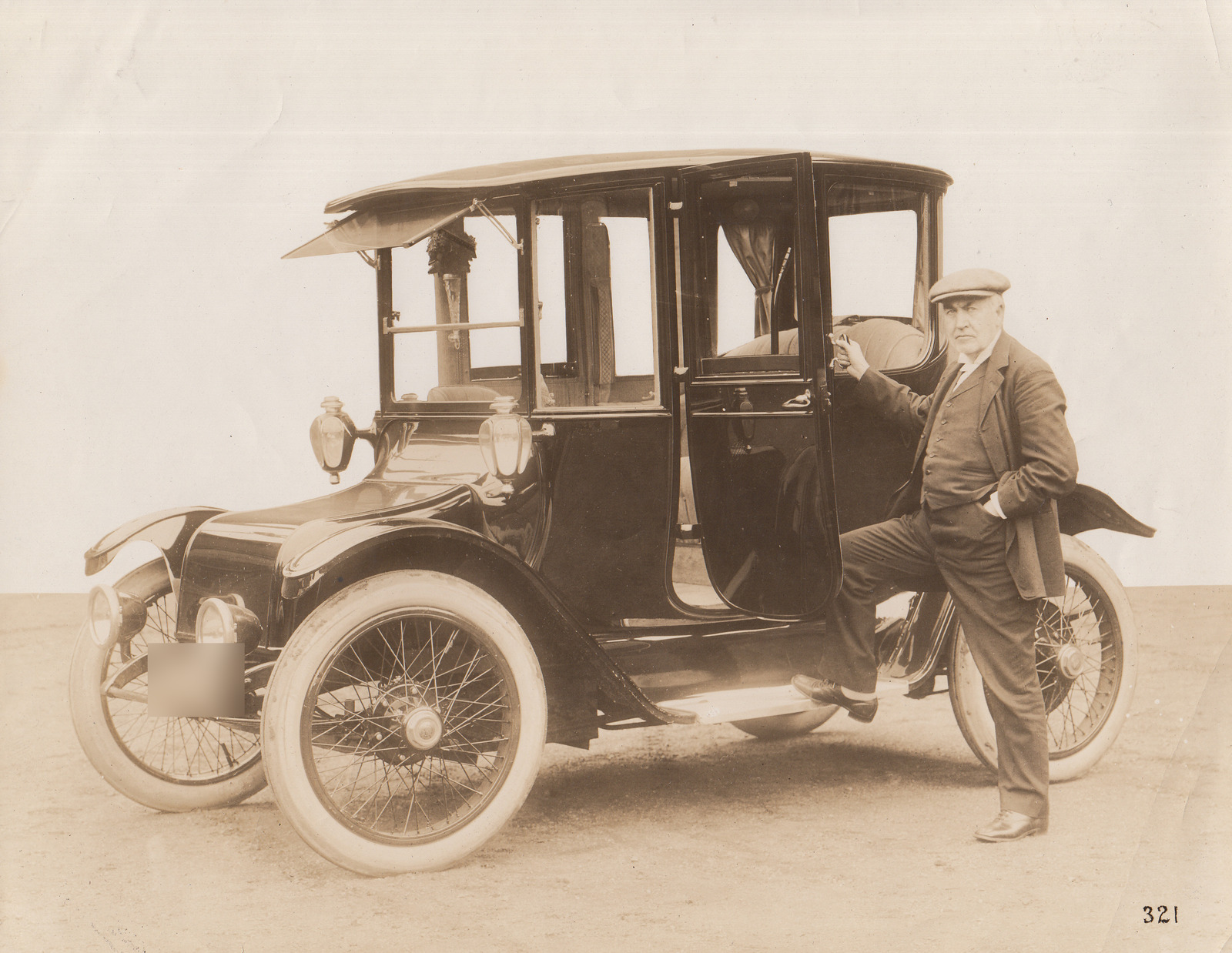 Thomas Edison standing beside the open door of his enclosed 1914 Detroit Electric Model 47 Brougham in a 1913 photograph; the historic registration is blurred.